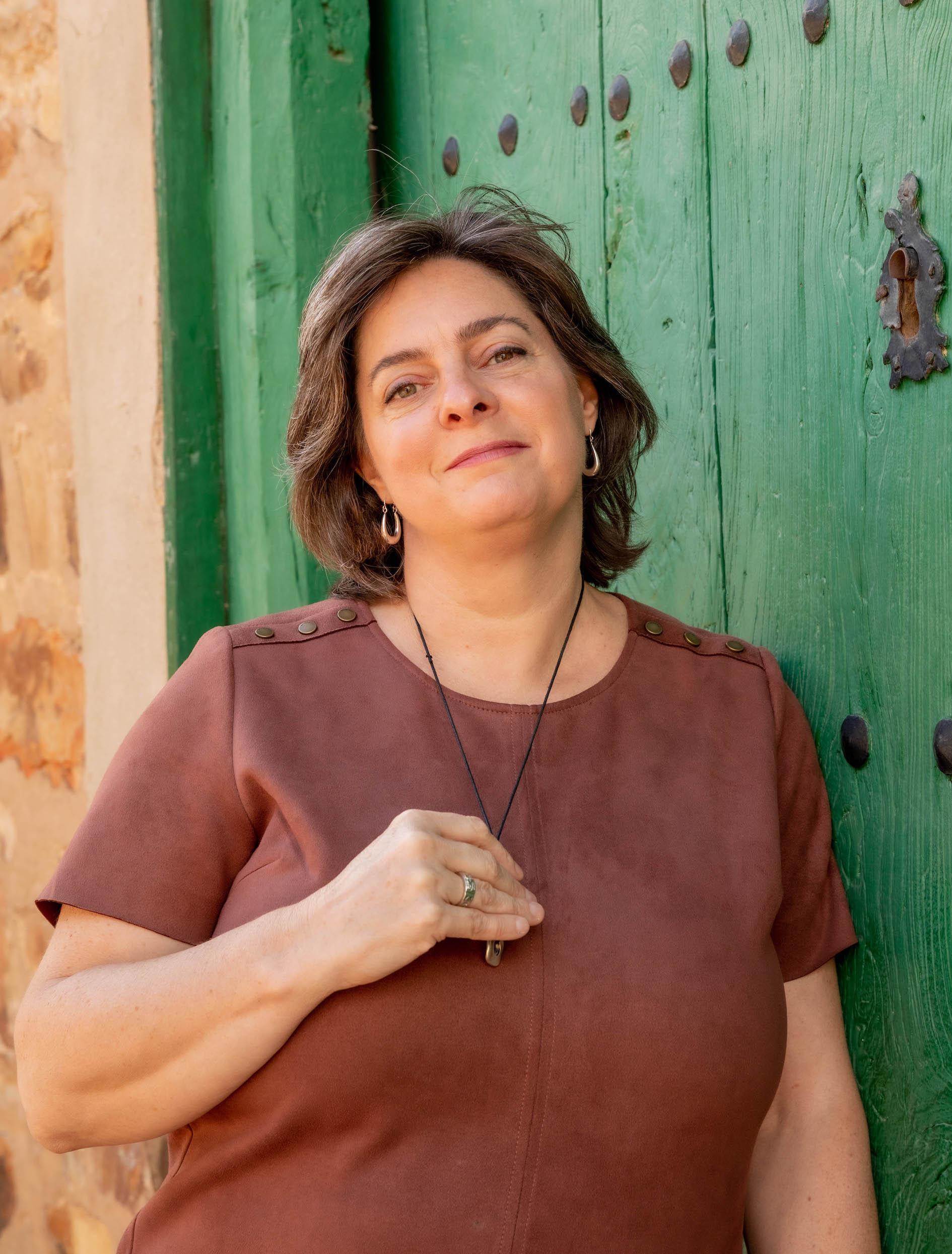 Christi Byerly, founder of Awaken is looking at the camera, holding a pendant necklace and smiling.